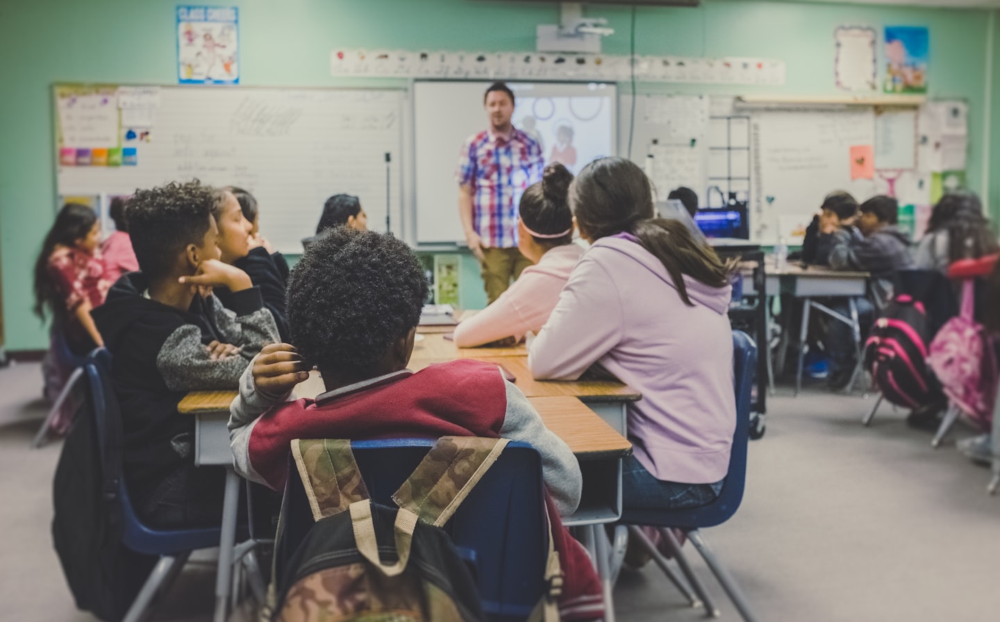 Students in a classroom being taught by their teacher.